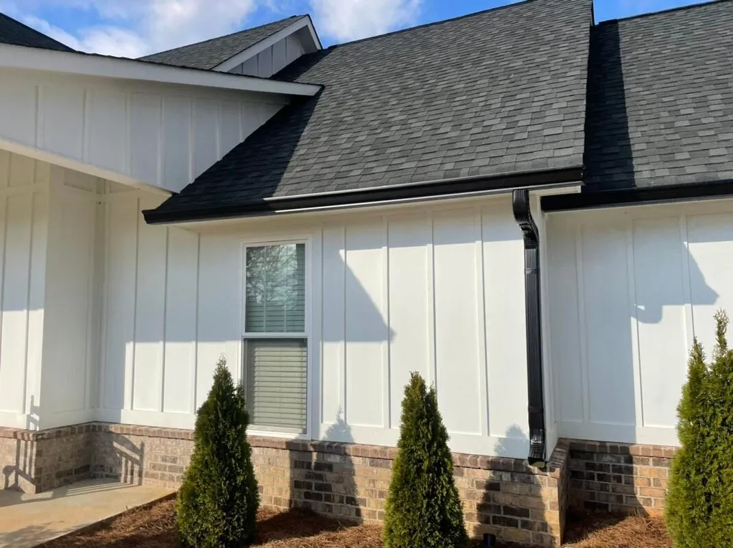 Black gutter and downspout run installed along a dark shingle roofline on a white board-and-batten West Georgia home