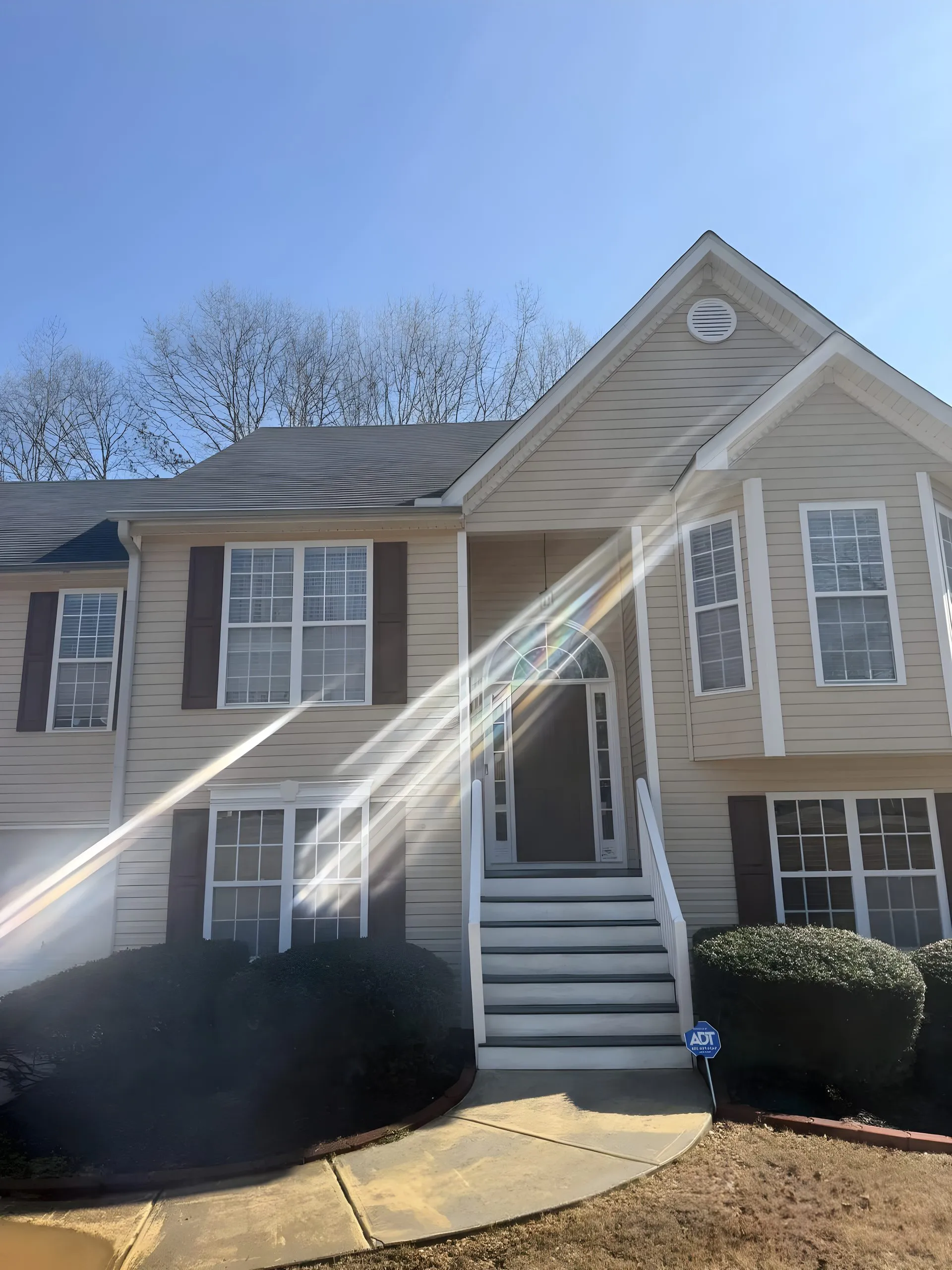Sunlit two-story home in Villa Rica with clean tan siding, brown shutters and a bright entry walkway after a house wash