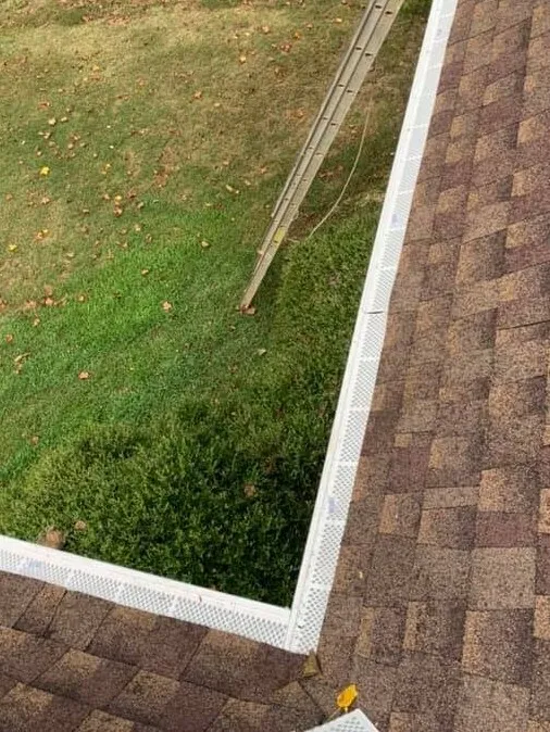 Rooftop view down a white gutter run with mesh guard installed, turning a corner at the roof edge in West Georgia