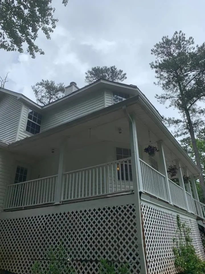 Two-story white farmhouse with a covered porch, white railings and lattice skirting, clean bright siding under pine trees