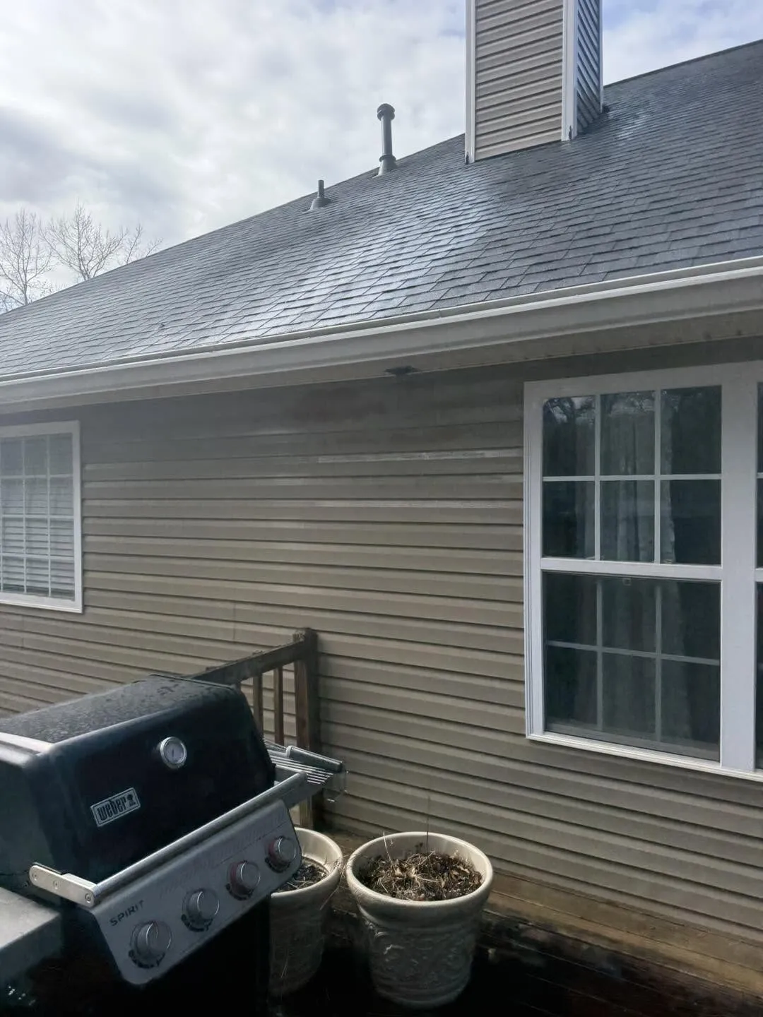 Shaded asphalt shingle roofline above grimy tan siding in Villa Rica, before a wash