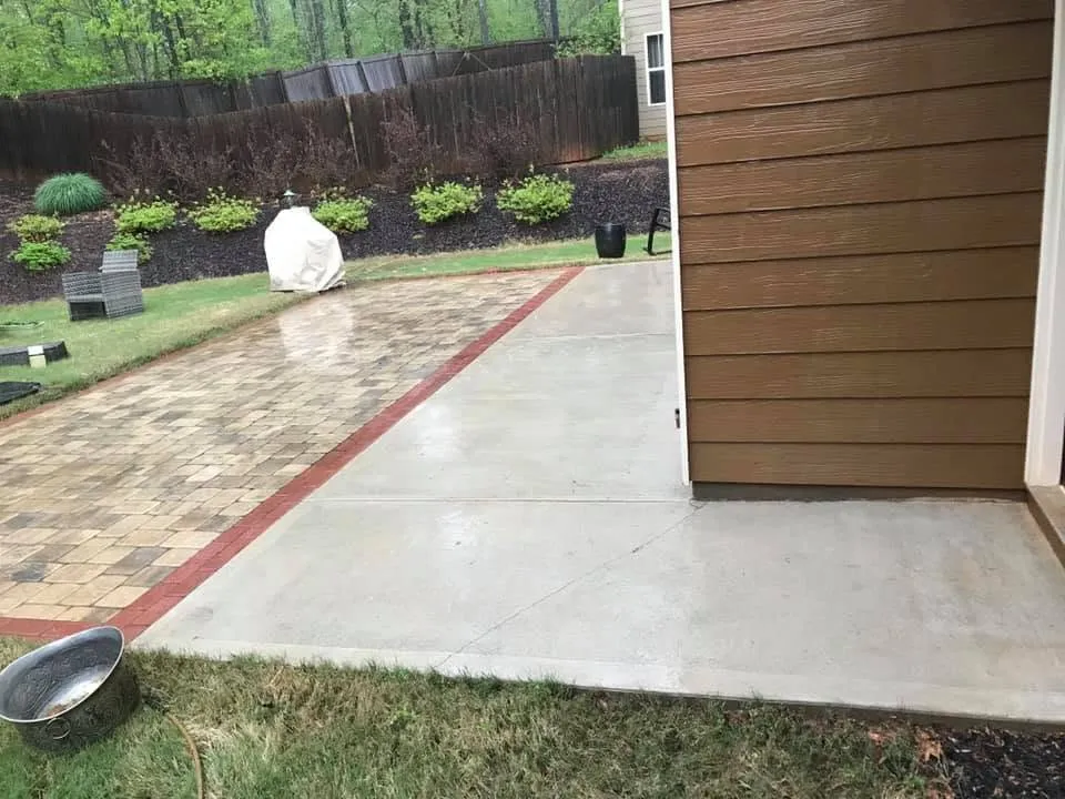 The same paver patio washed uniform and clean, crisp red brick border, wet concrete apron alongside